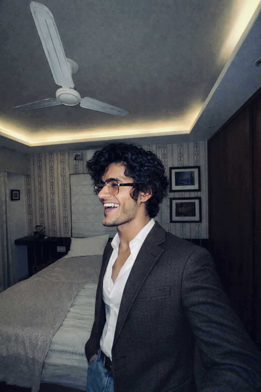 Atharva Sharma in tailored tweed blazer and glasses laughing indoors