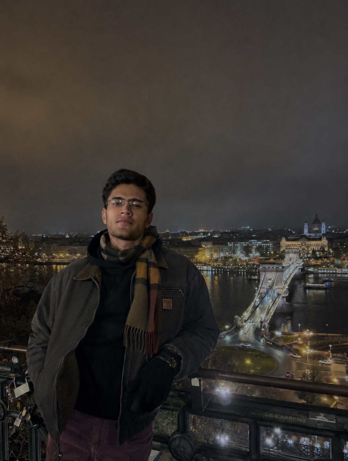 Atharva Sharma overlooking European city bridge with plaid scarf